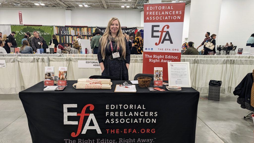 Volunteer behind a table covered with a black EFA logo drape and laid out with brochures and marketing materials
