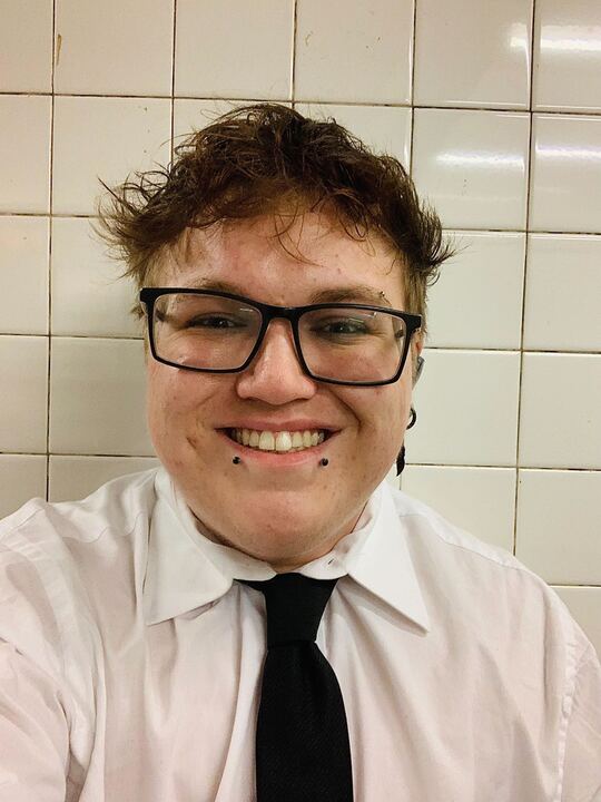 Smiling person with glasses dressed in a white shirt and black tie