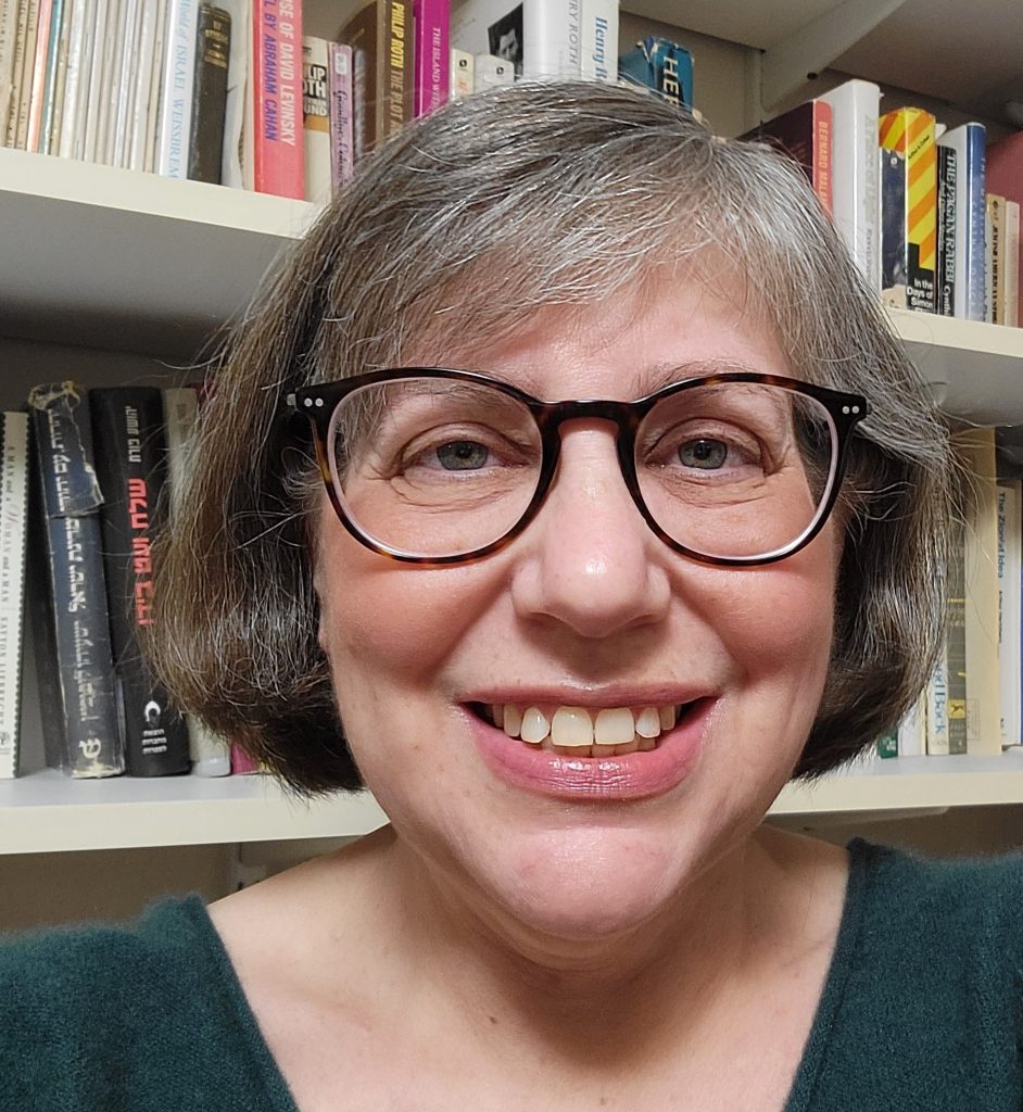 Woman with glasses and a dark green sweater in front of a bookcase.